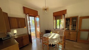 A kitchen with wooden cabinets, a dining table with chairs, a chandelier, and a view through the open door.