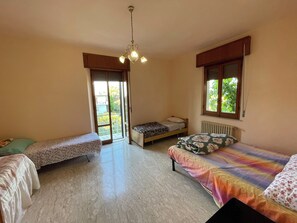 Quarto com duas camas de solteiro, ventoinha no teto, radiador e janela com vista para o verde.