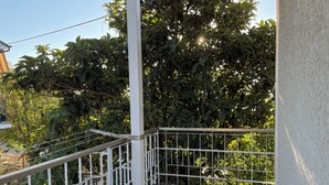 A balcony with a metal railing, a tiled floor, and lush greenery in the background.