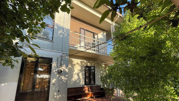 A two-story building with a balcony, a door, and a small tree in the foreground.