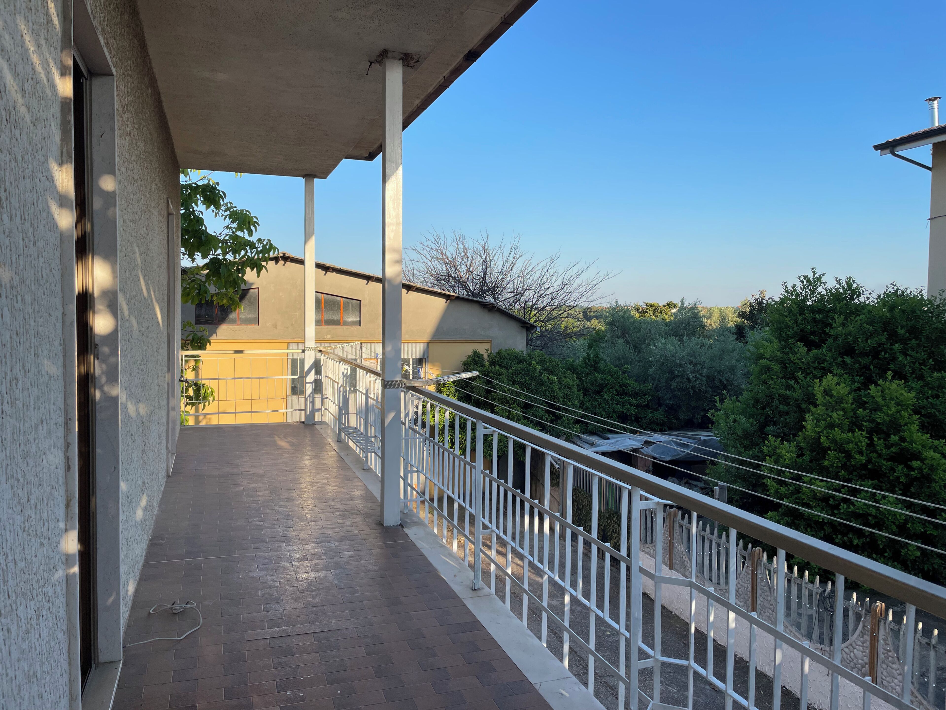 A balcony with a concrete floor, white railings, and a view of a building and greenery.