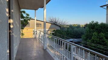 A balcony with a concrete floor, white railings, and a view of a building and greenery.