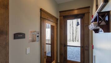 A hallway with a wooden door labeled "SAUNA," a thermostat, and a sign with a list of amenities.