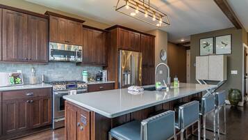 A modern kitchen with wooden cabinets, stainless steel appliances, a central island with bar stools, and a decorative light fixture.
