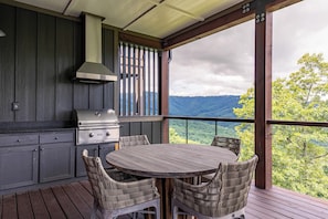 A covered outdoor kitchen with a grill, dining table, and wicker chairs. - AEA - 198 Ramblestone NC (Banner Elk)