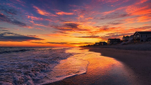 Ein Strand mit Wellen, einem Sonnenuntergang und Strandhäusern.