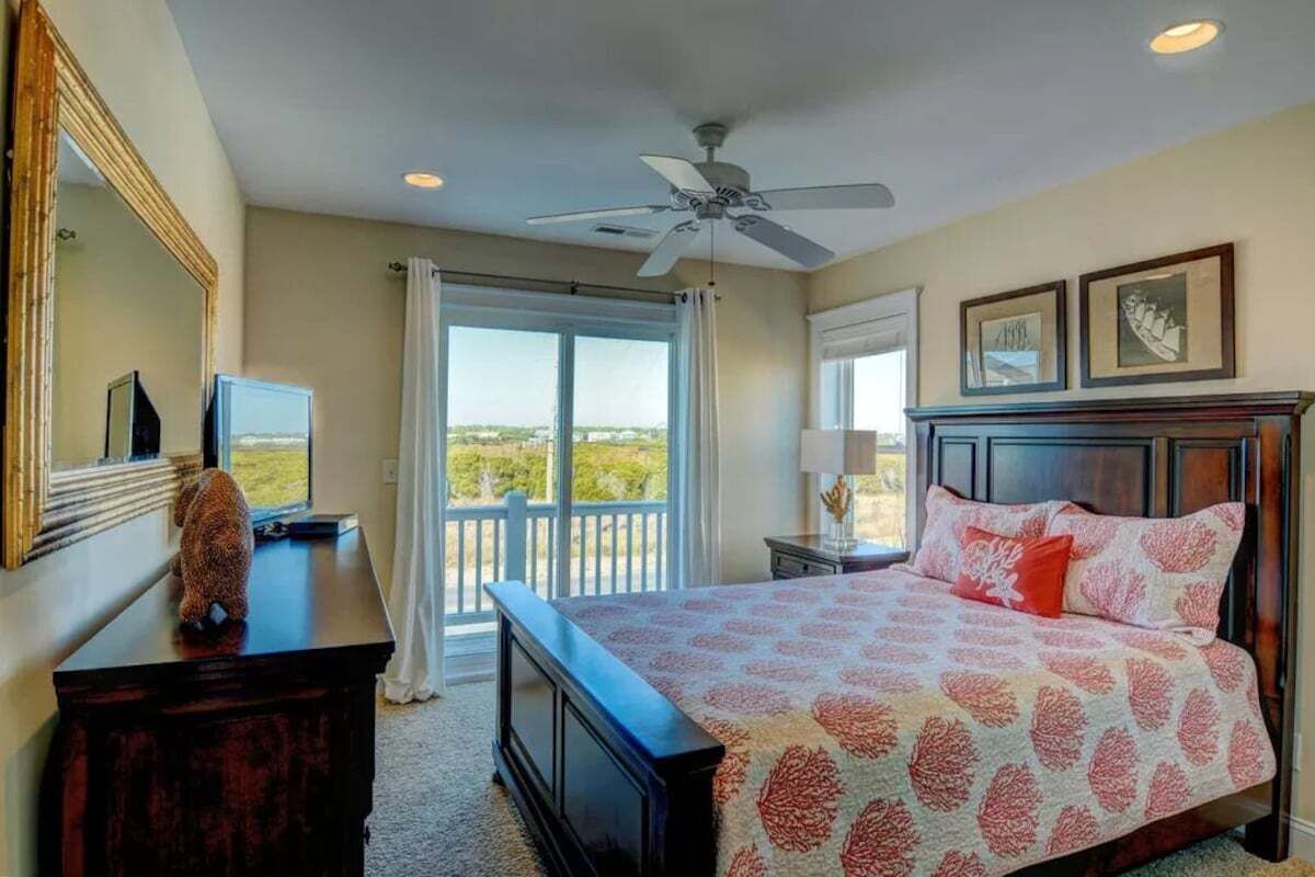 A bedroom with a bed, a ceiling fan, a dresser, a TV, and a balcony with a view.