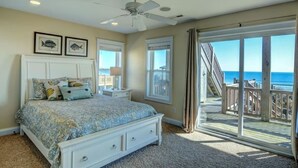 Ein Schlafzimmer mit Bett, Deckenventilator, Nachttisch und großem Fenster mit Meerblick.