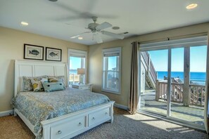 A bedroom with a bed, a ceiling fan, a nightstand, and a large window with a view of the ocean.