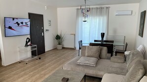 Una sala de estar moderna con un sofá seccional, una mesa de centro, un televisor, un comedor y una planta en maceta.