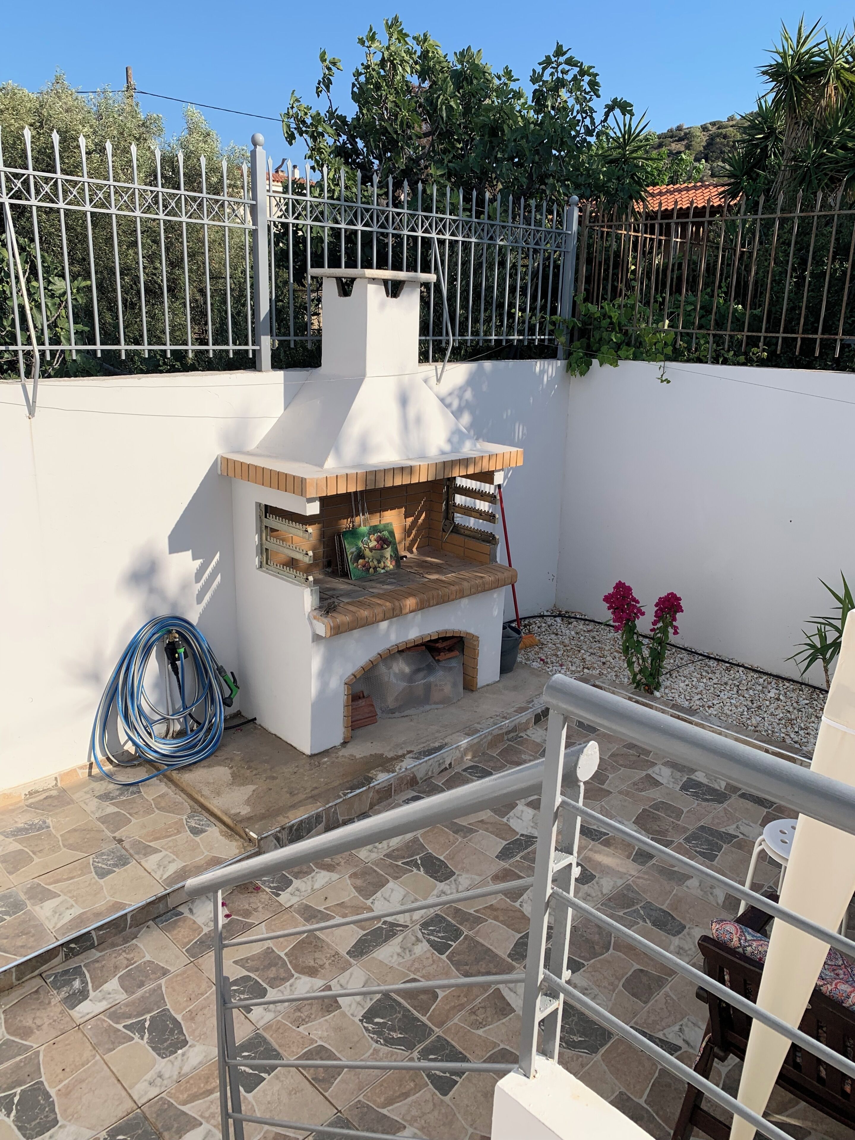 Un patio con una parrilla, una manguera y una silla.