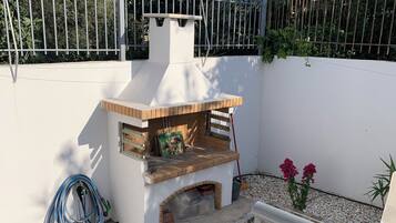 Un patio con una parrilla, una manguera y una silla.