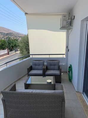 Ein Balkon mit Korbmöbeln, einem Glastisch und einem grünen Gartenschlauch.