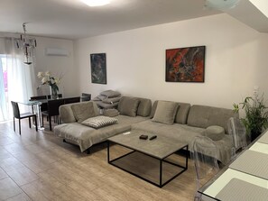 Ein modernes Wohnzimmer mit einer Eckcouch, einem Glastisch und einem Essbereich mit Tisch und Stühlen.