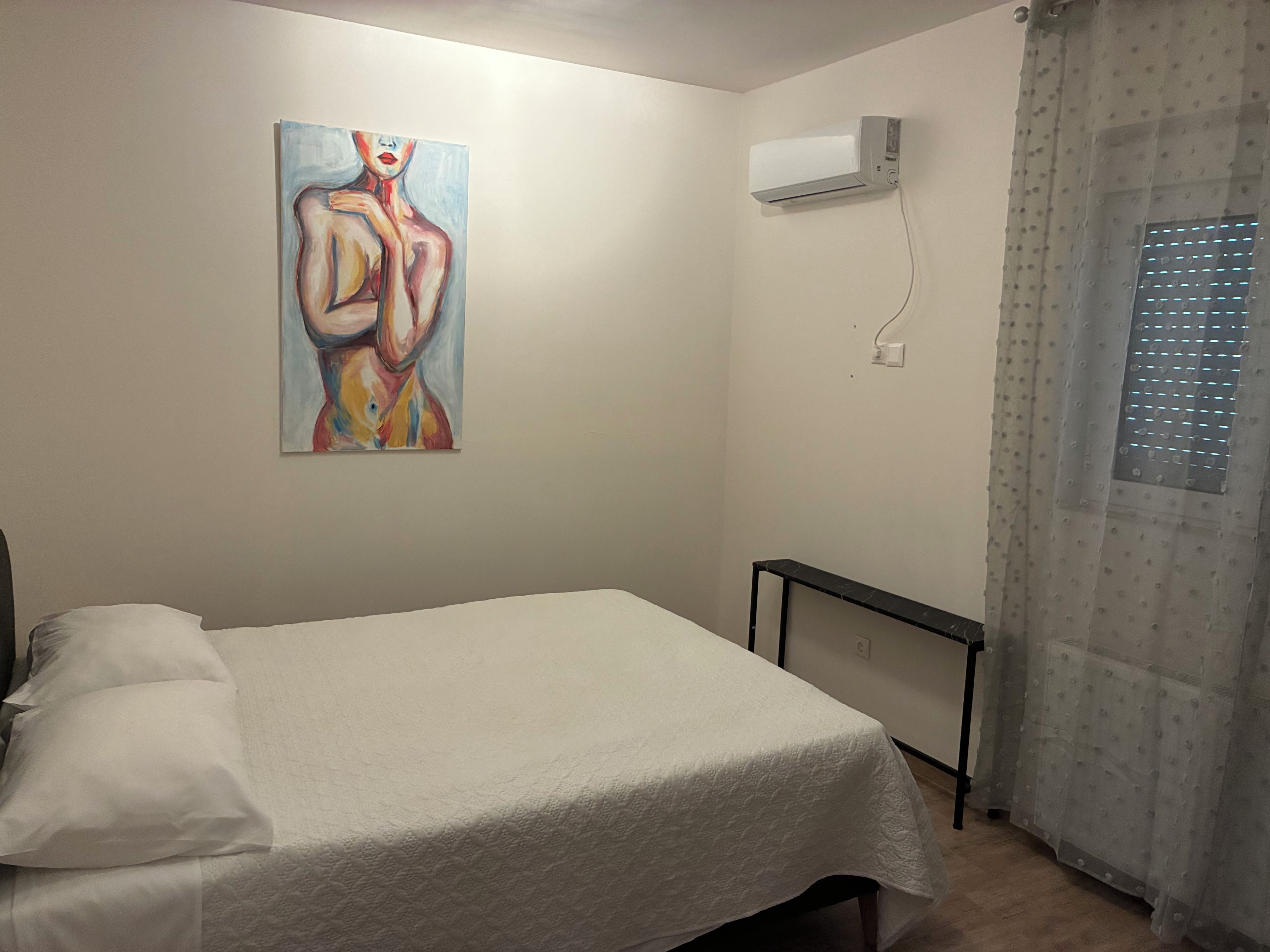 Ein Zimmer mit einem Bett, einem Wandbild, einer Klimaanlage und einem Fenster mit Vorhang.
