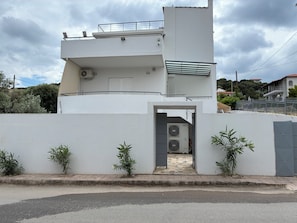 A modern two-story building with a flat roof, a balcony, and a gated entrance.