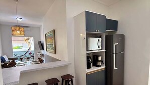 A compact kitchen with a built-in refrigerator, a coffee maker, and a dining area with stools. - Your Home in Ubatuba - Comfort Near the Beach! (Ubatuba)