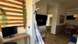 A living room with a wooden slat wall, a hammock, a flat-screen TV, a desk with a chair, and a dining area with chairs. - Your Home in Ubatuba - Comfort Near the Beach! (Ubatuba)