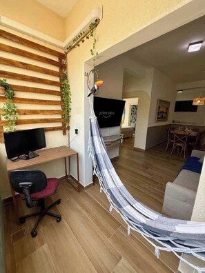Ein Wohnzimmer mit einer Wand aus Holzleisten, einer Hängematte, einem Flachbildfernseher, einem Schreibtisch mit Stuhl und einem Essbereich mit Stühlen.
