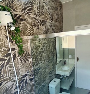 Ein Badezimmer mit einer blattmusterigen Wand, einem Spiegel, einem Waschbecken und einer weißen Mülltonne.