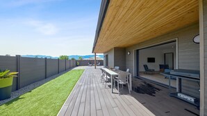Eine moderne Terrassenanlage mit Holzboden, einem Essbereich mit Stühlen und Tisch sowie Bergblick im Hintergrund.