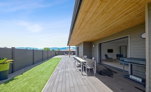 Un patio moderno con terraza de madera, mobiliario exterior y vistas a la montaña.