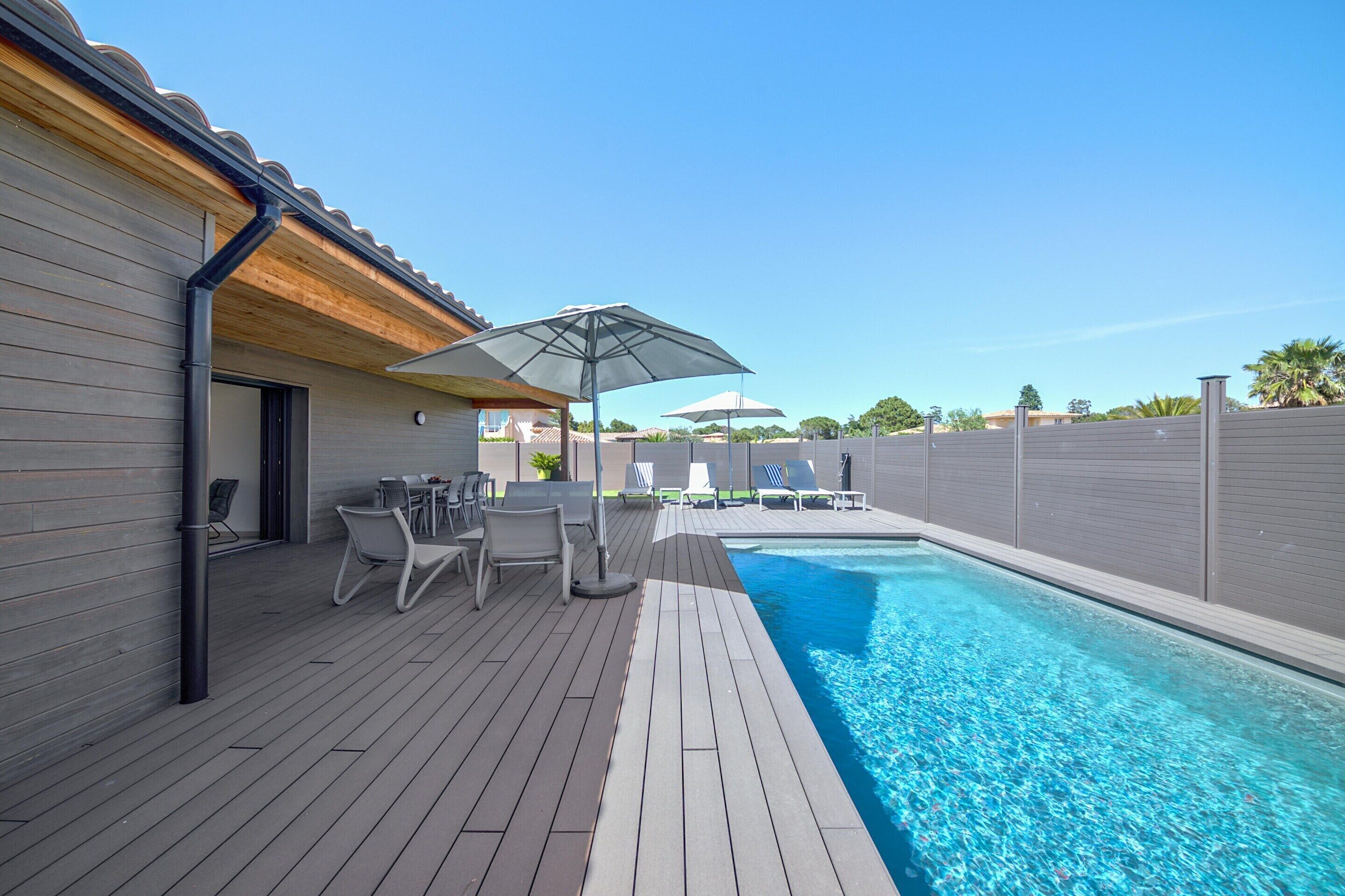 En swimmingpool med træterrasse, liggestole og parasoller.