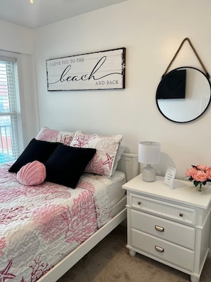 A bedroom with a bed, a bedside table, a mirror, and a wall decoration.