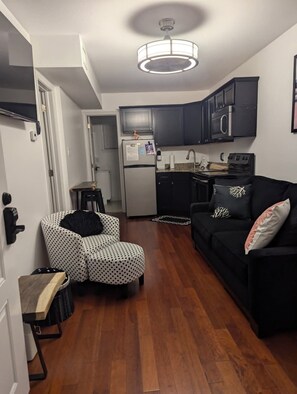 A compact living space with a kitchenette, a dining area, and a seating area with a sofa and ottoman.