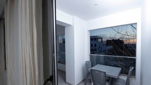 A balcony with a table and chairs, a view of buildings, and a door with a curtain. - sandra 6 (Marsa)