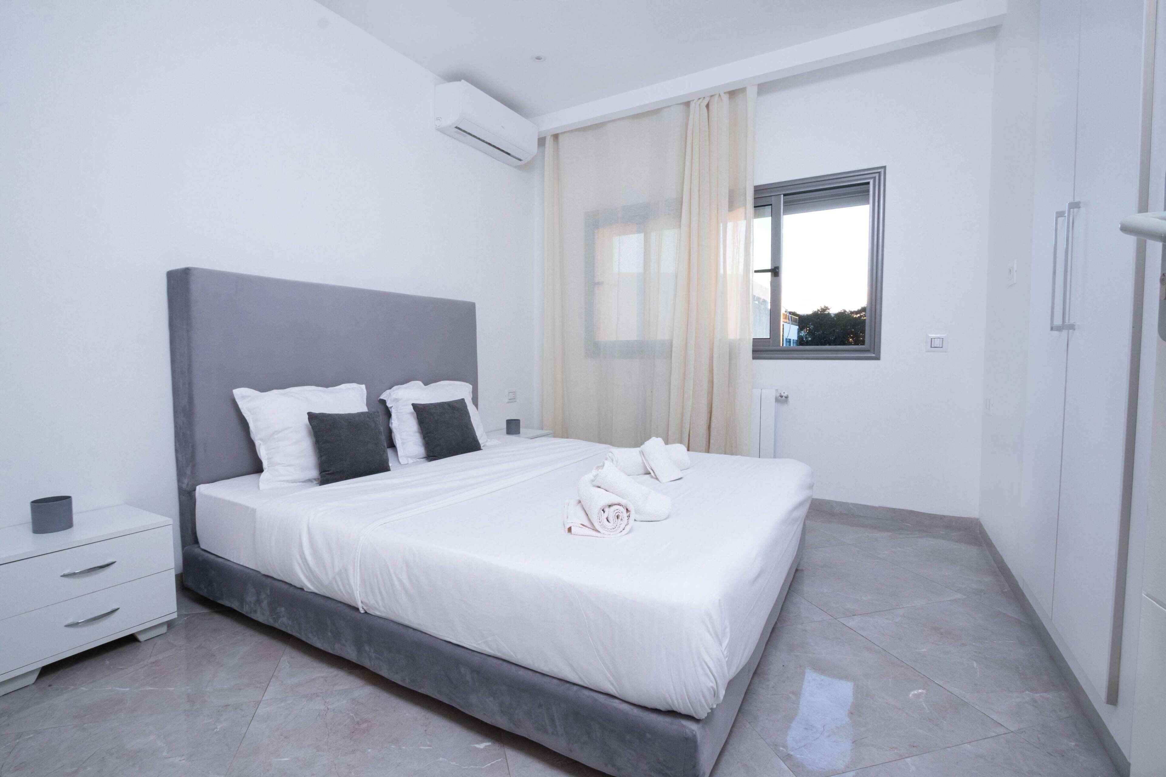 Un dormitorio moderno con una cama grande, una mesita de noche y una ventana con cortinas.