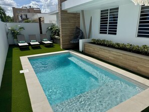 A swimming pool with a tiled edge, surrounded by artificial grass and a wooden planter with small plants. - 5 Bedroom Pool Villa Walk to Beach with Solar Backup (San Juan)