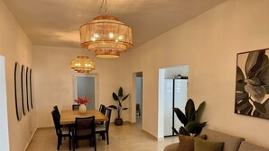 Un salon moderne avec un canapé, une table à manger et des chaises, un lustre et une grande plante.