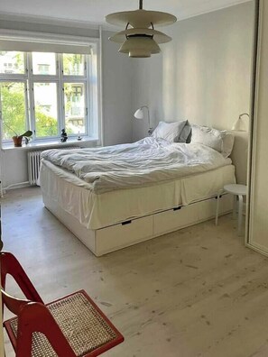 Ein Schlafzimmer mit Bett, Fenster, Heizkörper, Stuhl und Lampe.