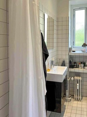 Ein Badezimmer mit einem weißen Waschbecken, einem Spiegel, einem Handtuchhalter, einem Fenster und einer Heizung.