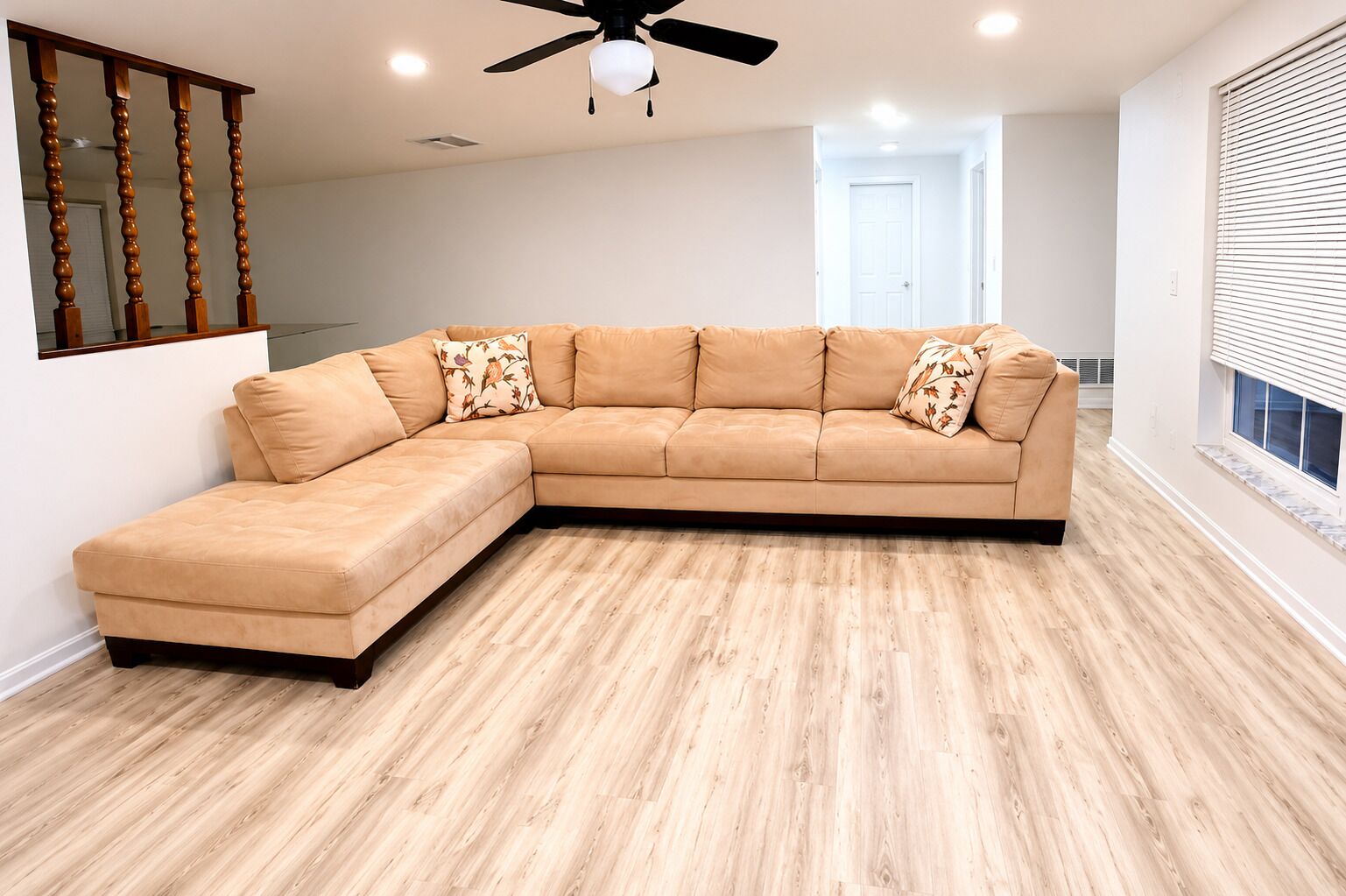 A L-shaped sectional sofa with floral pillows, a ceiling fan, and a wooden floor.