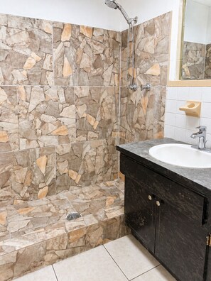 A bathroom with a stone wall, a bathtub, a sink, and a mirror. - Beautiful 3-bedroom house with AC in charming Port Richey (Port Richey)