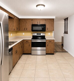 A modern kitchen with wooden cabinets, stainless steel appliances, and a tiled floor. - Port Richey Palms (Port Richey)