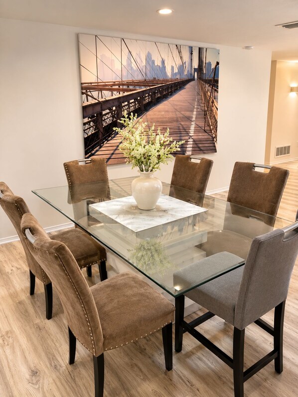 A modern dining area with a glass table, six chairs, and a cityscape painting on the wall.