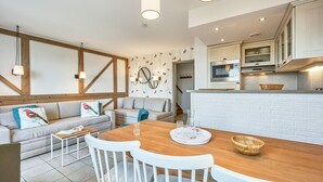 Una cocina moderna con armarios blancos, una mesa de comedor de madera y una zona de estar con sofá y sillas.