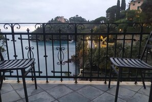 Un balcon avec deux chaises, une rambarde en métal et une vue sur une étendue d’eau et des bâtiments.