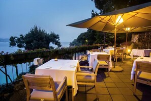 An outdoor dining area with tables and chairs, a large umbrella, and a view of the water.