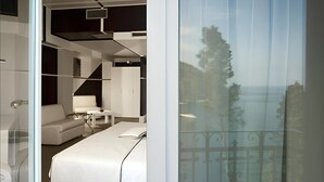 Une chambre moderne avec un lit, un canapé blanc, une petite table et un balcon doté d’une balustrade.