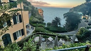 Un hôtel en bord de mer doté d’une terrasse avec vue sur la mer, d’une allée sinueuse et d’une végétation luxuriante.