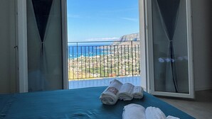 Une chambre avec un lit, deux portes coulissantes ouvertes et une vue sur un paysage côtier.