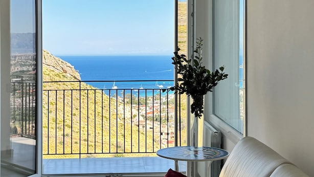 Un salon moderne avec un canapé, une petite table et une vue sur la mer depuis un balcon.