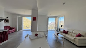 Un salon moderne avec un canapé rouge, un canapé blanc, une table basse et un coin repas doté d’une table rouge.