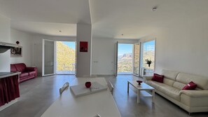 A modern living room with a red sofa, a white sofa, a coffee table, and a dining area with a red table. - Villa Perla Blu Mondello, breathtaking sea views and relaxation (Palermo)