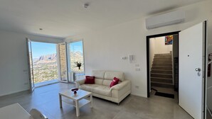 Un salon moderne avec un canapé, une table basse et une vue sur un paysage montagneux, visible à travers de grandes fenêtres.