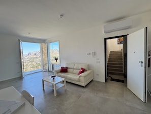 A modern living room with a sofa, a coffee table, and a view of a mountainous landscape through large windows. - Villa Perla Blu Mondello, breathtaking sea views and relaxation (Palermo)